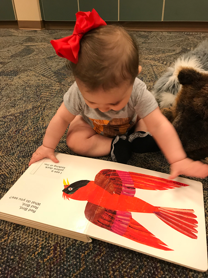 A baby reading a board book on the floor