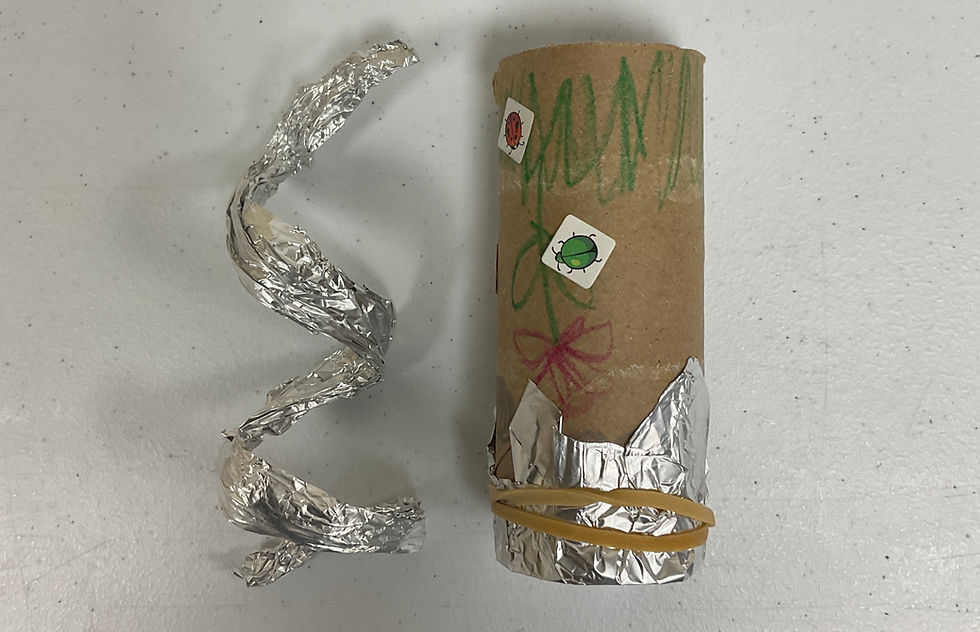 A piece of foil curled into a coil next to a cardboard tube with one end covered by a foil cap.