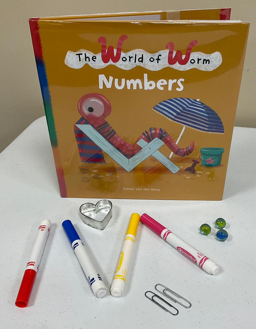 The book shows a worm reclining in a beach chair with a large umbrella, bucket, and shovel nearby