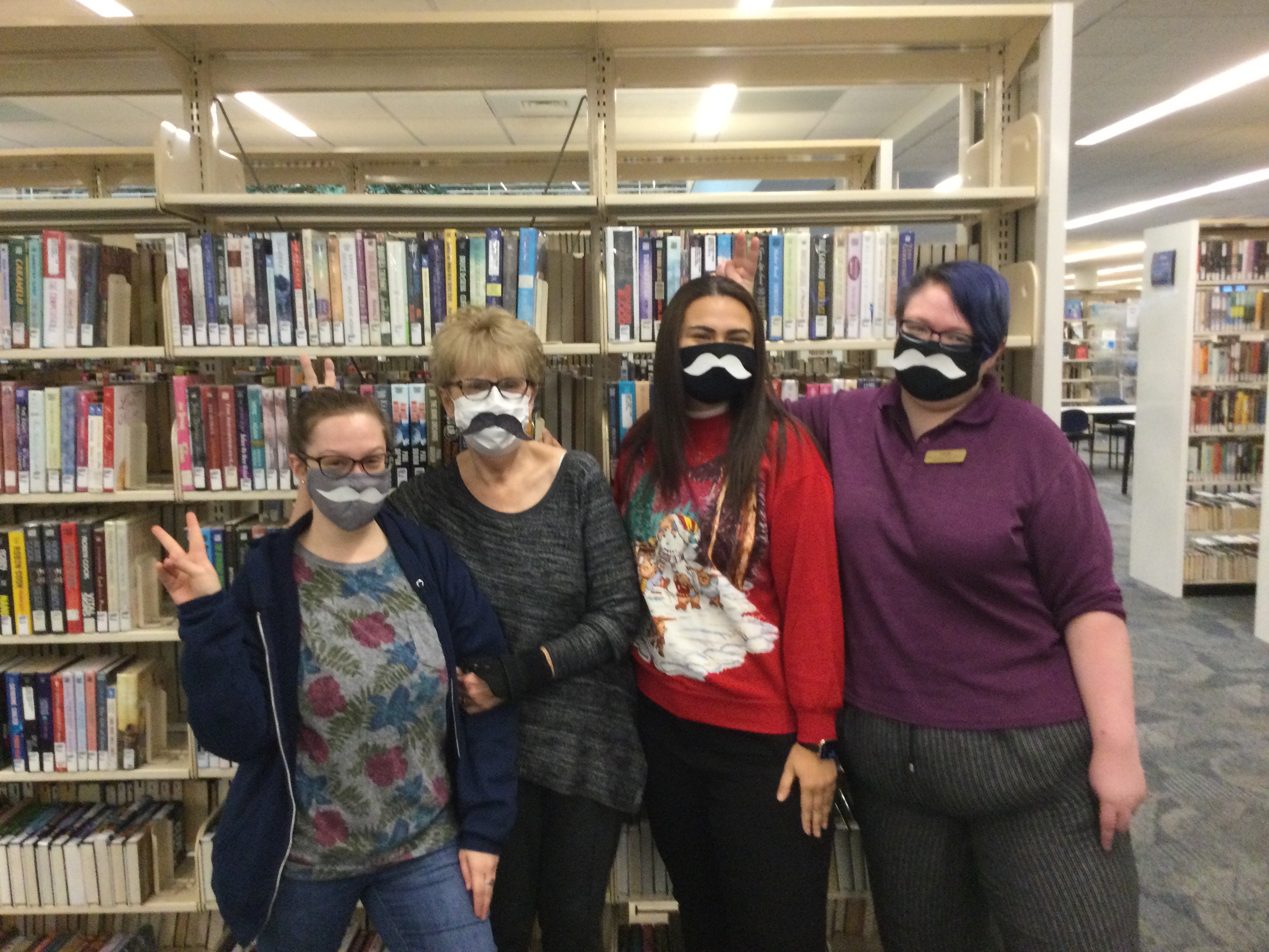Four library workers posing with mustaches attached to the front of their face masks