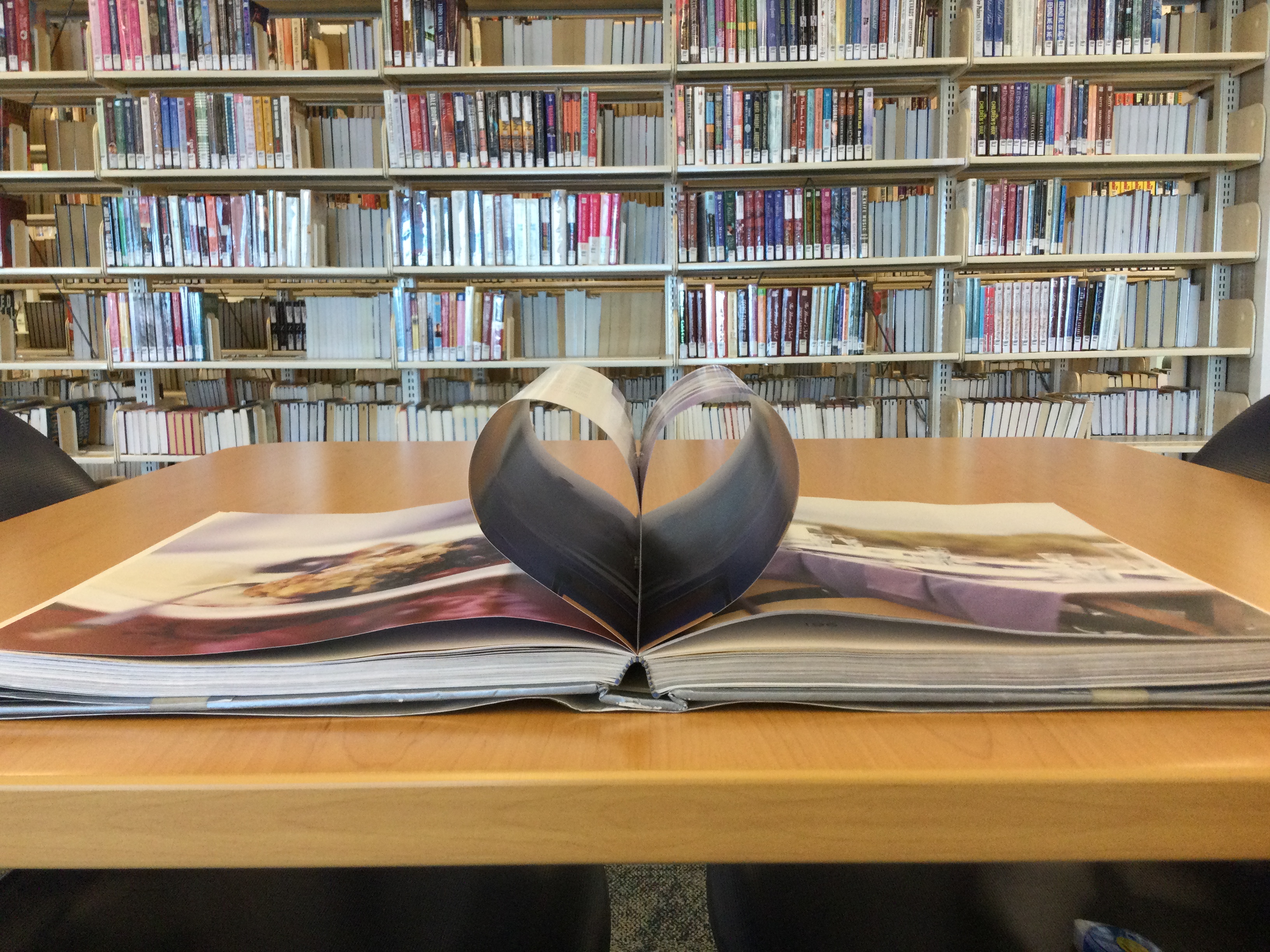 A book open on a table with its center pages folded in to resemble a heart