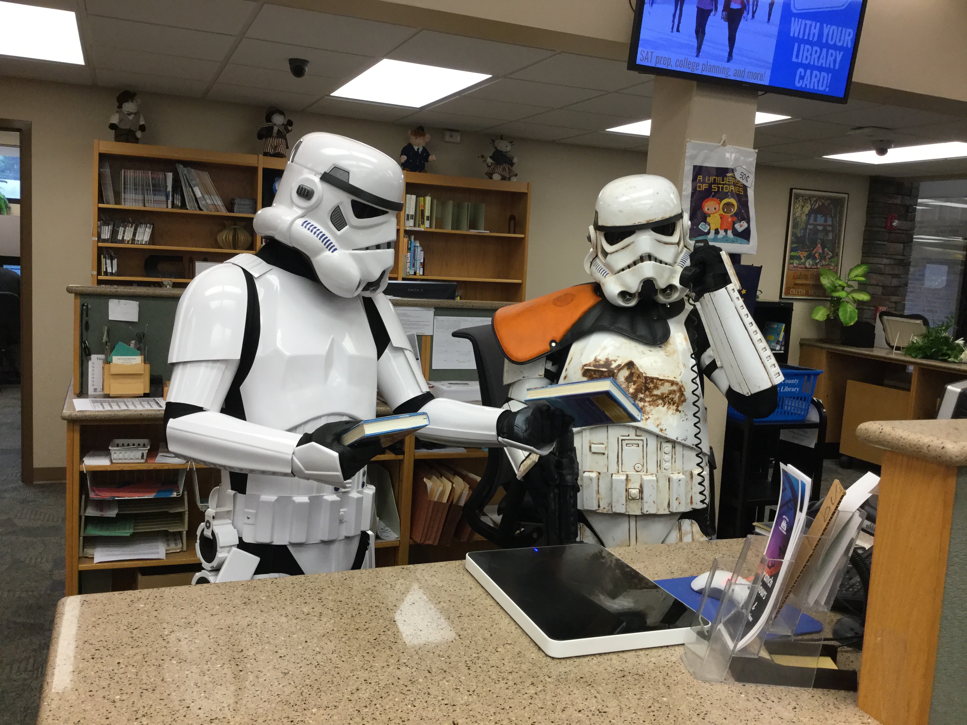 Two stormtroopers behind a library desk. One is on the phone, the other is offering a book for his inspection