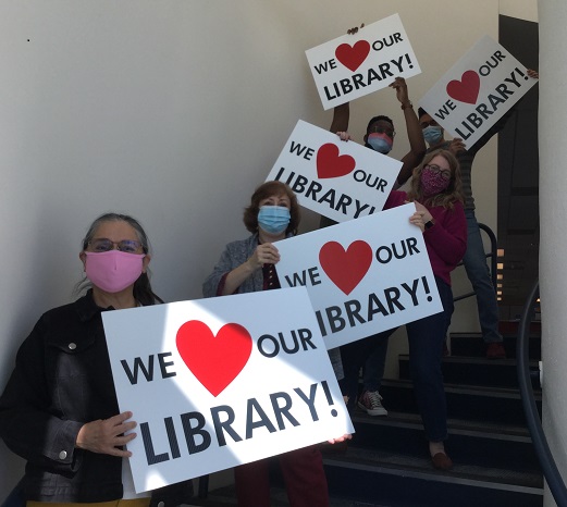 Photo of people standing at different levels on stairs holding signs that say we heart our library